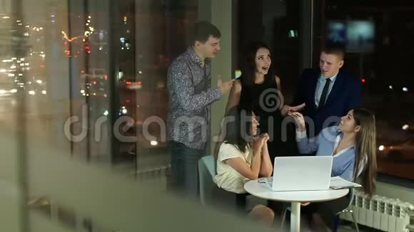 在玻璃办公室工作人员拿着笔记本电脑站在桌子周围微笑着交流视频的预览图