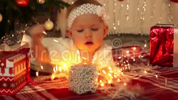 美丽的小女孩穿着白色连衣裙躺在地板上的节日圣诞树和许多礼物1920x1080视频的预览图