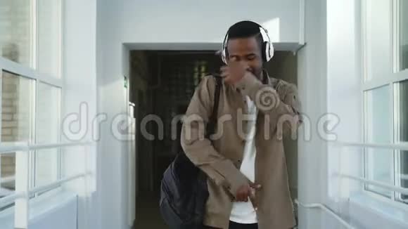 年轻英俊的非裔美国学生在白色的大学走廊里跳舞注意到他的朋友视频的预览图