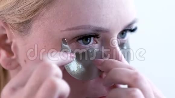 女人在眼睛下面施加了一片清爽的补水面膜在浴室内部眼睛下面有胶原蛋白垫的女性视频的预览图