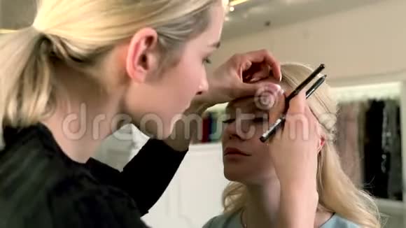 专业化妆师将眼线涂在美容院的金发女人身上美妆时尚理念视频的预览图