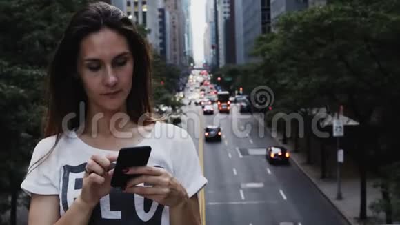 美国纽约桥上站着的年轻漂亮女人的肖像使用智能手机视频的预览图
