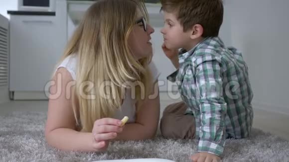 母亲的温柔快乐的蹒跚学步的孩子和母亲一起吃食物在室内地板上揉鼻子视频的预览图