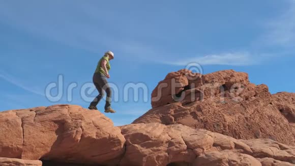 运动成熟的女人小心地沿着峡谷的红岩走下去视频的预览图