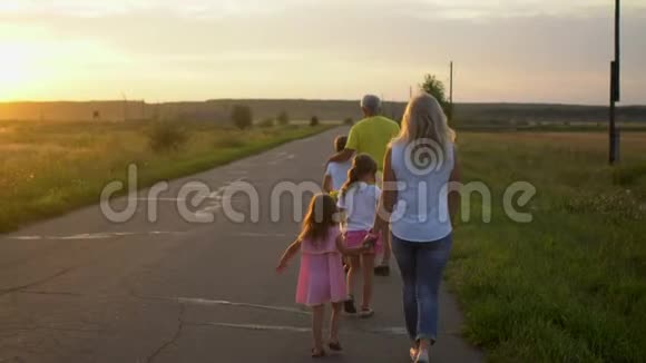 幸福成熟的父亲和母亲带着三个孩子在日落时在农村上路快乐的家庭享受大自然视频的预览图