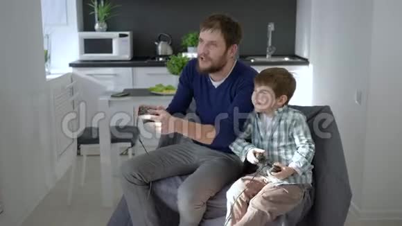 快乐的周末快乐的爸爸和孩子坐在椅子上玩电子游戏视频的预览图