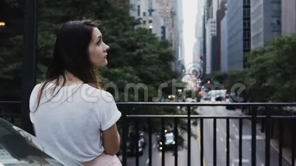 在美国纽约年轻美丽的女人站在桥上看着交通道路视频的预览图
