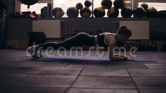 一个年轻的黑发女孩站在木板上穿着黑色运动服耐力健身健康的生活方式视频的预览图