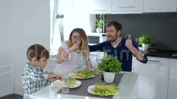 健康的食物快乐的爸爸妈妈和儿子一起吃厨房里刚准备好的饭菜视频的预览图
