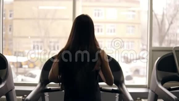 在跑步机上跑步时一个长着深色头发的活泼女孩的背部镜头印支视频的预览图