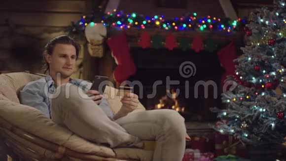 年轻的长发男子在圣诞夜使用智能手机和信用卡在线购物视频的预览图