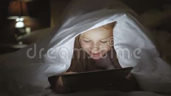 年轻女子妈妈和女儿一起在平板电脑上看有趣的电影在毯子下面笑有趣的妈妈和视频的预览图