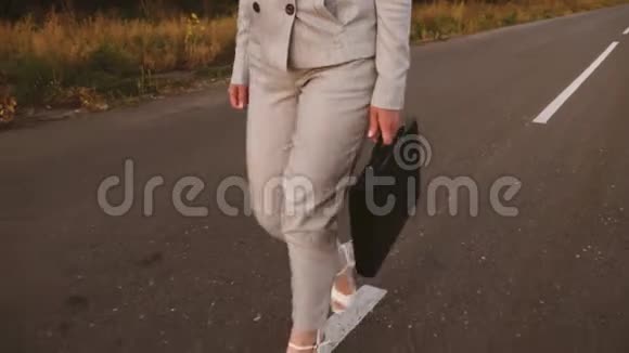 瘦削的商人女人手里拿着黑色公文包走在沥青上穿着浅色西装和白色鞋子的女孩视频的预览图
