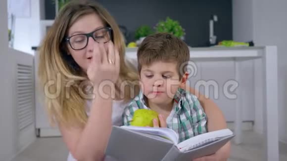 快乐的童年妈妈戴着眼镜给手里拿着苹果的孩子读童话视频的预览图