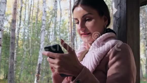 秋天森林里的快乐女人在电话上交谈在智能手机上发送信息在手机上读一些东西视频的预览图