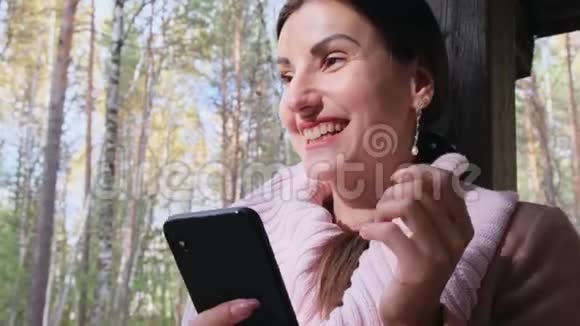 秋天森林里的一个开朗的女人在电话上交谈在智能手机上发送信息在手机上读一些东西视频的预览图
