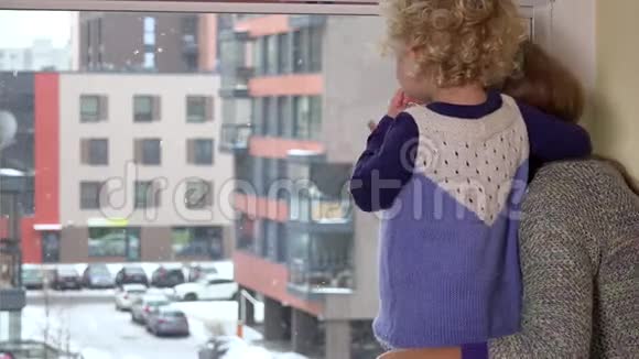 女人透过窗户向孩子展示雪花冬天降雪视频的预览图
