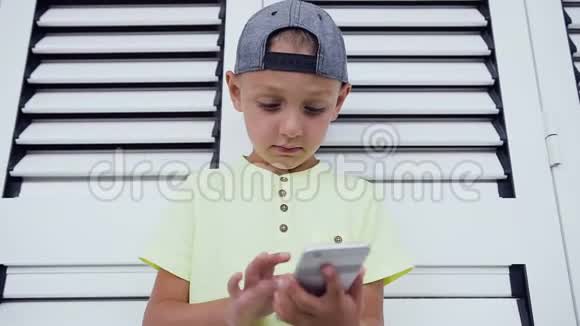 少年戴着帽子在智能手机上玩游戏孤立在白色的门背景上儿童玩智能手机视频的预览图