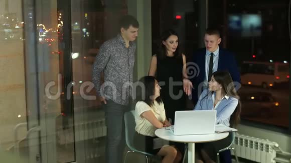 在玻璃办公室工作人员拿着笔记本电脑站在桌子周围微笑着交流视频的预览图