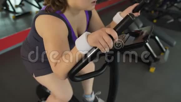 肥胖妇女呼吸困难坐在健身房里的固定自行车上视频的预览图