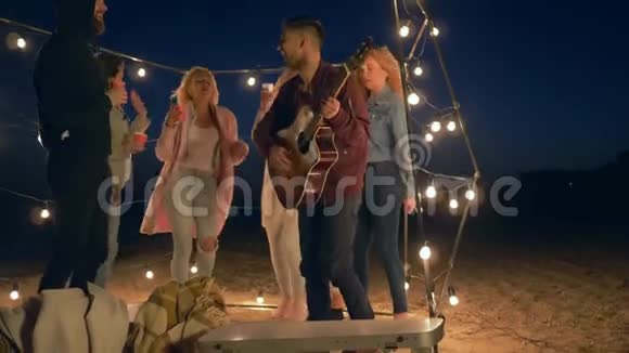 海滩派对快乐的男人和女孩与吉他音乐舞蹈和笑声在花环照明视频的预览图