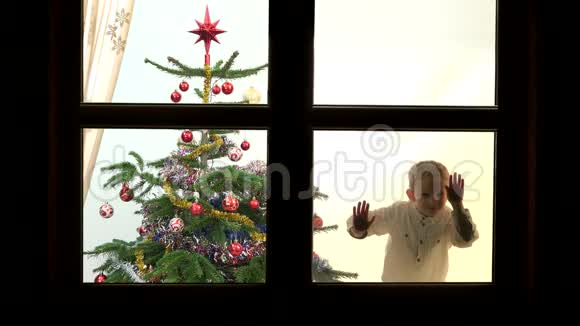 一幅有趣的儿童舞蹈画靠近圣诞树在窗户上寻找和等待圣诞老人视频的预览图