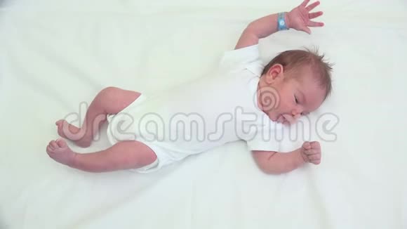 可爱的新生手和腿活跃的婴儿躺在床上体操视频的预览图