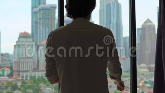 一个男人的剪影用摩天大楼把俯瞰市中心的窗户的窗帘拉上视频的预览图
