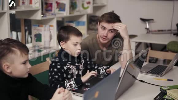 20的年轻男教师向两个小男孩讲解一些东西教他们如何使用笔记本电脑视频的预览图