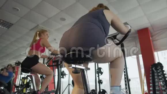 肥胖女性在体育俱乐部固定自行车上工作的全貌视频的预览图