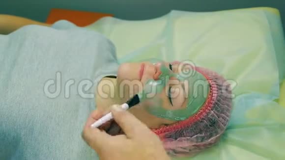 时光飞逝化妆师的男人的手在女人的脸上用刷子刷上一个液体的绿色面具视频的预览图