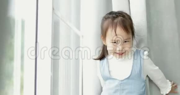 快乐的亚洲女孩在家里微笑着在窗帘后面捉迷藏视频的预览图