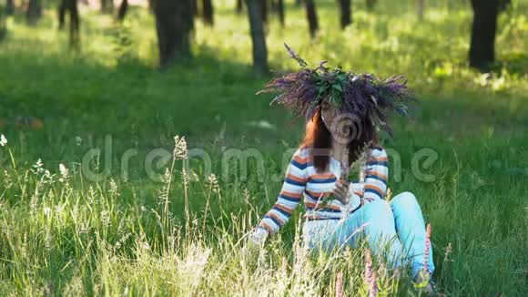 美丽的女孩她的头上有一个来自矢车菊的花在森林的一片草地上收集野花视频的预览图