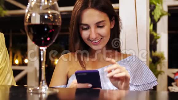 为坐在酒吧的漂亮女孩提供最新的智能手机和美酒视频的预览图