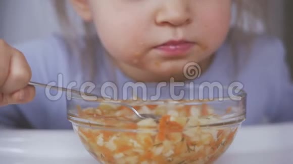 一个小女孩吃了一勺蔬菜汤弄脏了脸仔细地看电视视频的预览图
