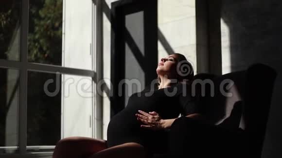 漂亮的孕妇坐在椅子上太阳光照在女人身上她穿着黑色的紧身衣视频的预览图