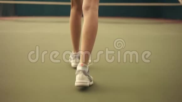 一名年轻的运动网球运动员在覆盖的球场区域向网走的背面镜头慢动作视频的预览图