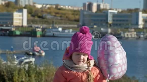小女孩戴着粉红色的帽子带着气球坐在河港上一边旅行一边微笑视频的预览图