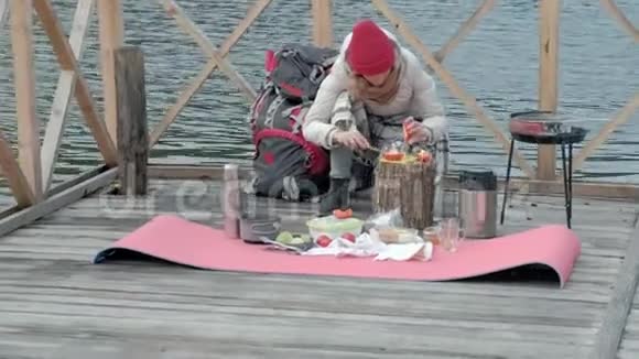 一位穿着暖和的衣服的女游客在河岸附近的一座桥上背着一个背包筛着蔬菜准备吃饭视频的预览图