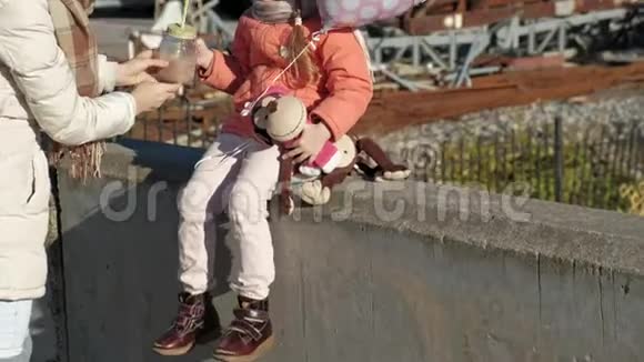 小女孩戴着一顶粉红色的帽子带着一个气球坐在河港上旅行微笑着女人妈妈给喝了一杯视频的预览图