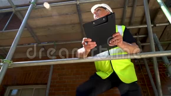 建筑工地的男建筑工人在剪贴板上写字并用手机交谈视频的预览图