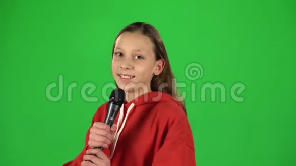 在演播室绿色背景下对着麦克风唱歌的女孩视频的预览图
