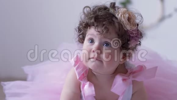 一个不高兴的小女孩卷发穿着粉色连衣裙在白色的工作室里摆姿势视频的预览图