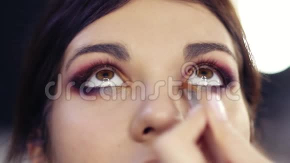在美丽的黑发女孩的眼睛内角添加一些金色眼影创造完美的色彩视频的预览图