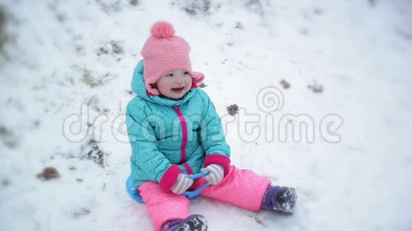 穿着温暖的雪服和粉红色针织帽的幼儿女孩坐在Saucer雪橇上可爱的儿童享受冬季户外活动视频的预览图