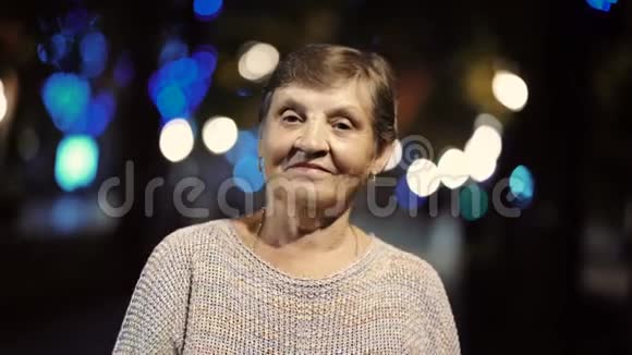 美丽的肖像微笑的老年妇女在夜晚灯光照亮街道高加索地区的祖母视频的预览图