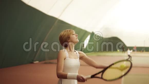 年轻女子肌肉发达穿着白色运动服在网球场用球拍击球涵盖的法院视频的预览图