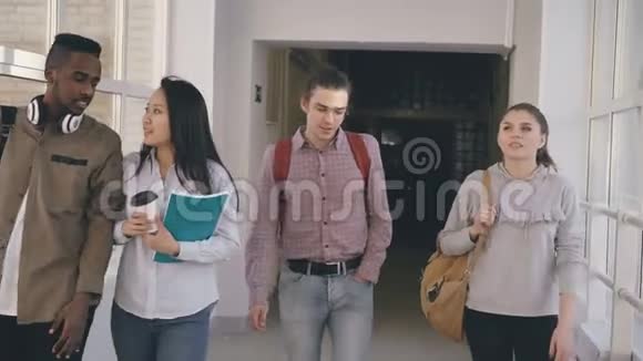 四个不同种族的同学正在大学里宽敞宽敞的玻璃走廊里微笑着走着视频的预览图