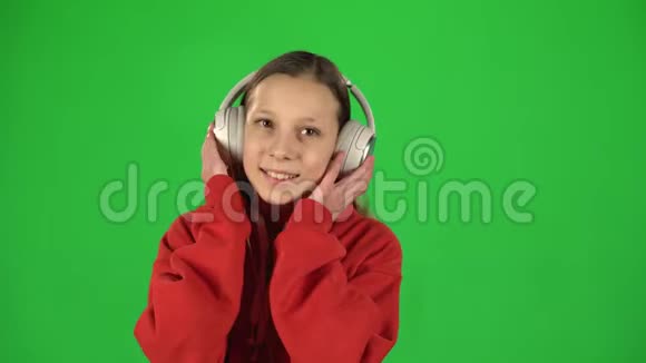 女孩听音乐戴着绿色背景的白色大耳机移动视频的预览图
