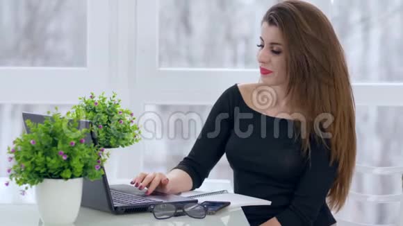 工作时间漂亮的女孩用笔记本电脑坐在现代办公室的桌子上视频的预览图